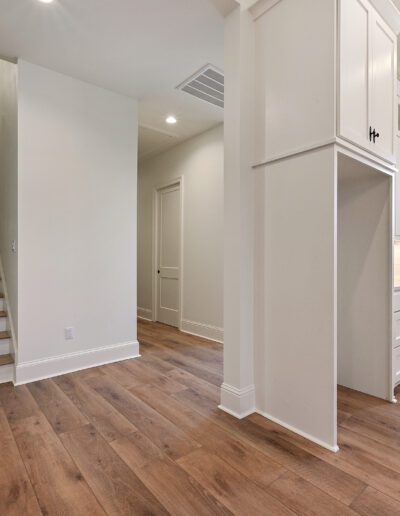 Newly renovated kitchen with white cabinetry and wooden floor extending to a staircase on the left.